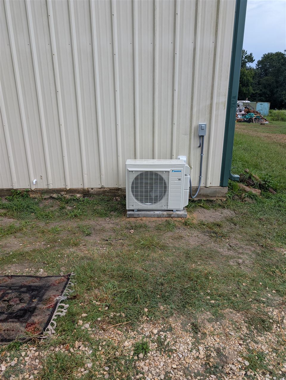 Daikin mini-split heat pump outdoor unit on a concrete pad beside a metal-sided building