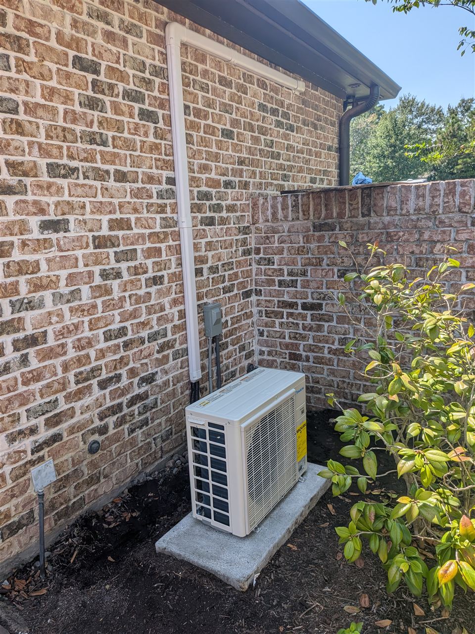 Daikin mini-split heat pump outdoor unit beside a brick wall with covered refrigerant lines